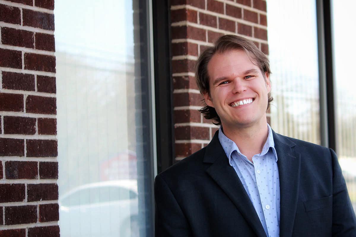 Nathan Lannan, smiling in a navy blazer in front of a brick building.